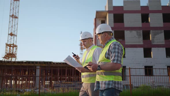 Waistup of Two Middleaged Male Builders Wearing Safety Clothing Standing at Construction Site Man