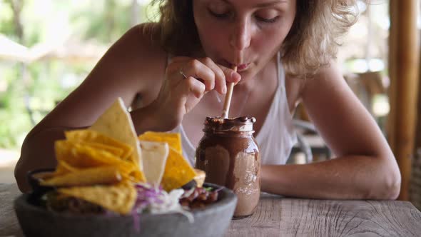 Beautiful Young Blonde Woman Enjoys Her Chocolate Milkshake While Having Lunch Alone at a Beach