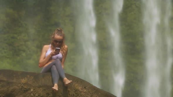 Girl in Sunglasses Texts Message Against Waterfall