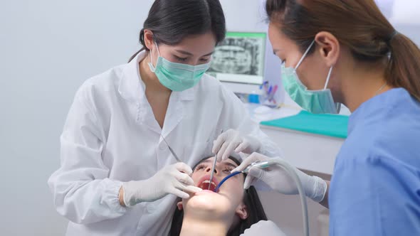 Asian female dentist using an explorer to examining young girl patient's teeth at dental clinic.