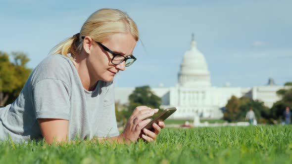 Happy Woman Lies on a Lawn Against the Background of the Capitol in Washington DC