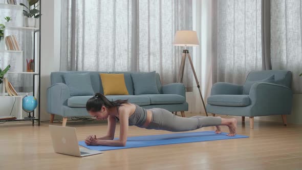 Athletic Female Doing Yoga In Forearm Plank Pose On The Mat At Home With Online Coach Via Laptop