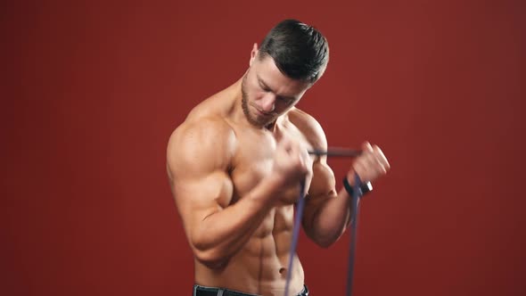 Muscular biceps of a man. Handsome bodybuilder doing workout against red background.