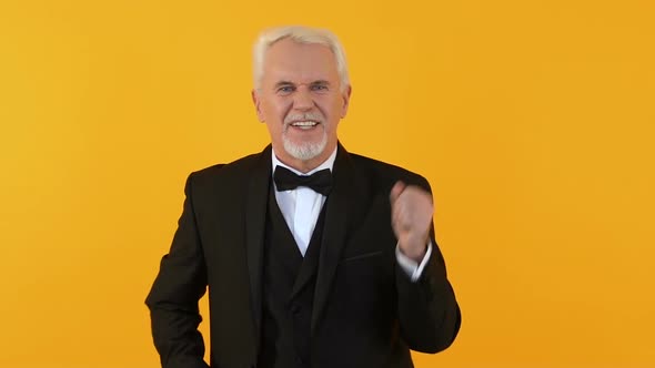 Playful Male Pensioner in Elegant Suit Dancing on Orange Background, Party Fun