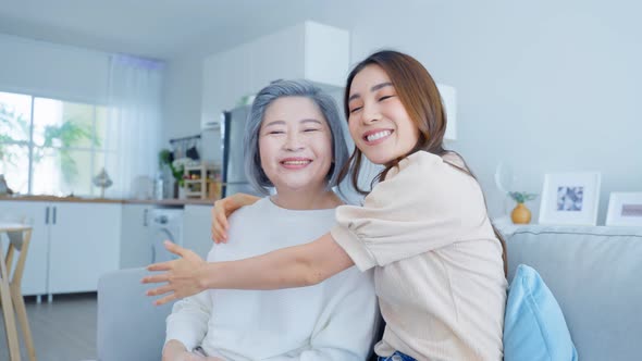 Portrait of Asian lovely family, young daughter hugging older mother at home in living room.