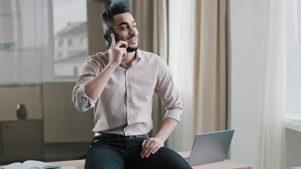 Smiling Arab Man Relaxed Male Entrepreneur Businessman Sitting Top of Table in Workspace Holding