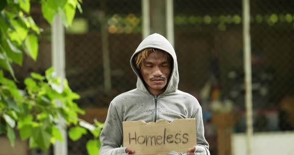 Homeless man holding homeless label and looking at camera.