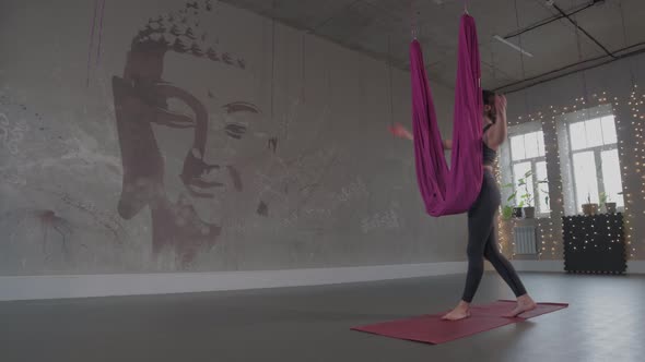 A Woman Walks to a Yoga Hammock in a Studio with a Picture of a Buddha on the Wall