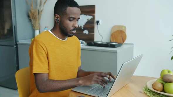 African American Guy Working From Home Using Laptop and Earphones During Covid19 Pandemic