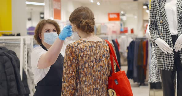 Seller in Safety Mask and Gloves Checking Temperature of Customer Before Entering Clothing Store