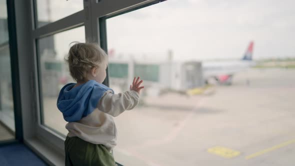 Little Boy Watching Planes at the Airport Standing in Silhouette with His Back to the Camera at a