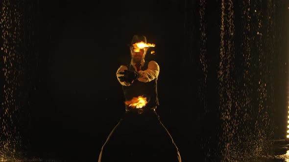 Male Fire Tamer in a Thrilling Close-up Fire Show in a Dark Studio in the Rain. A Silhouette of a