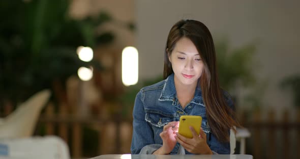 Woman use of mobile phone at outdoor cafe at night