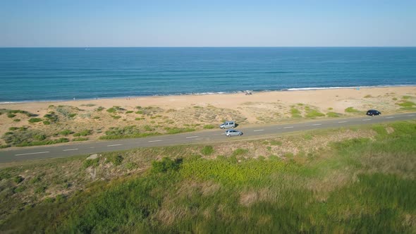 Panoramic View of Cars Driving Slowly on Sea Road with Sand Beach and Calm Sea Horizon with Blue Sky