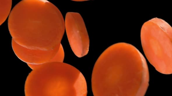 Closeup of Orange Juicy Carrot Slices Falling Diagonally on a Black Background