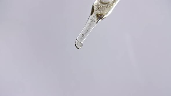 Cosmetic Pipette with Drops of Oil Close Up on Gray Background