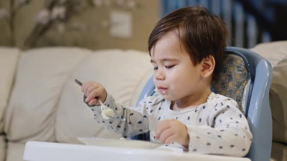 A Twoyearold Baby Eats Porridge on His Own Sits in a Feeding Chair