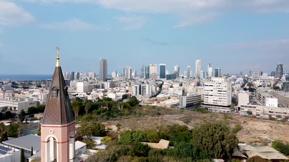 Aerial turn shot of a church steeple in front of city buildings, park and sky, on a sunny day.Israel