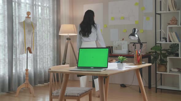 Green Screen Laptop Is On The Table While A Woman Walks Into Looking At The Sketch Paper On The Wall