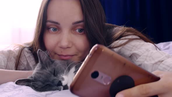 A Young Woman Takes a Selfie on a Smartphone with Her Cute Sleeping Cat the Pet is Graywhite the