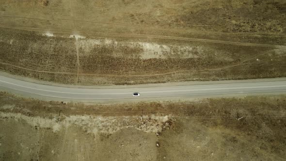 A White Car is Moving Along an Asphalt Road in the Mountain Steppe