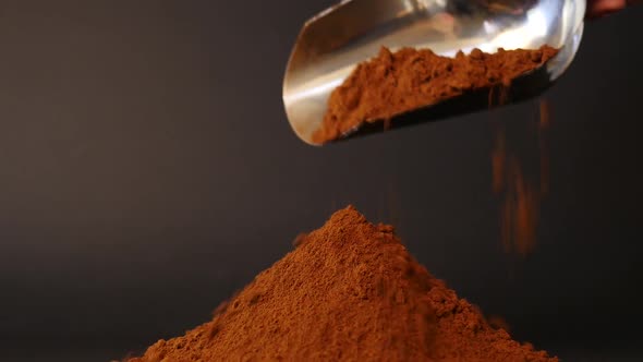 Finely ground coffee drips out of the scoop. Coffee powder on black background.