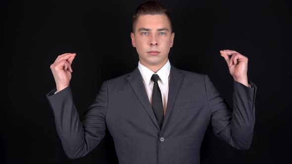 Young Businessman Snaps Fingers on Two Hands. Man in a Black Suit on a Black Background