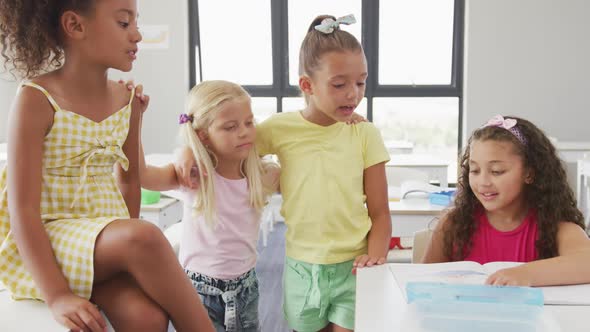 Video of happy diverse girls sitting at school desk, talking and laughing