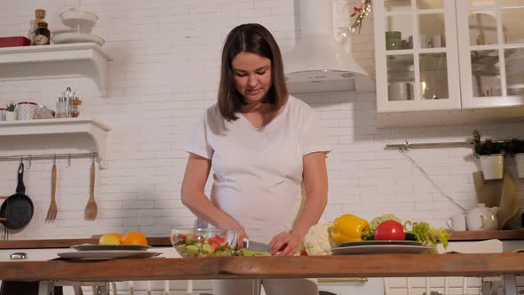 A Happy Pregnant Woman is Preparing a Vegetable Salad at Home in a Kitchen