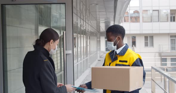 Young Businesswoman in Mask Receiving Package From African Courier Outside Business Center