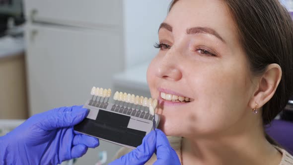 Dentist with Tooth Color Samples is Choosing Shade for Women Patient Teeth at Dental Clinic