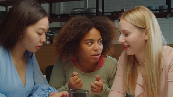 Joyful Multiethnic Girlfriends Whispering Gossip at Cafe