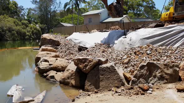 A excavator using a rock grab to build a boulder wall along a river