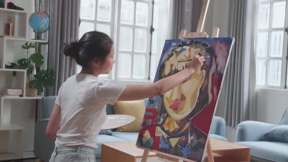 Side View Of An Asian Artist Girl Holding Paintbrush Mixed Colour And Painting On The Canvas