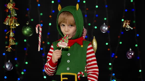 Kid Girl in Christmas Elf Santa Claus Helper Costume Licking Candy Lollipop Caramel Sweets