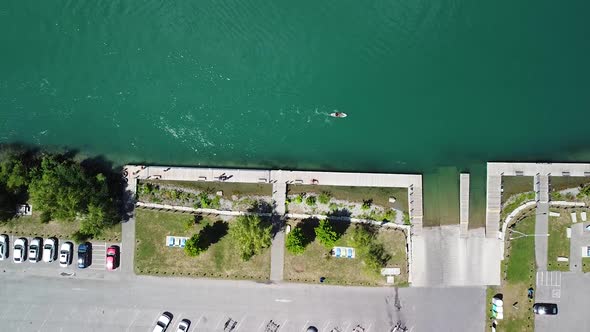 Aerial top down shot of parking cars beside river with person paddling on sup board during sunny day