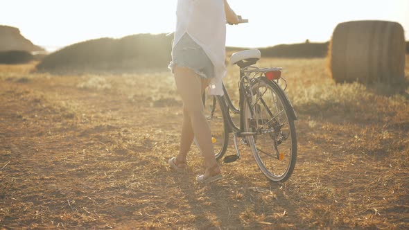 Back View Unrecognizable Slim Young Woman Walking with Bike in Sunrays Outdoors on Yellow