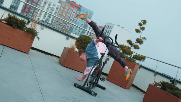 Athletic Girl Performing Aerobic Training Twine Exercises on Cycling Stationary Bike on House Roof