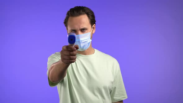 Man in Protective Mask Directs Electronic Noncontact Thermometer Into Camera Lens and Measures