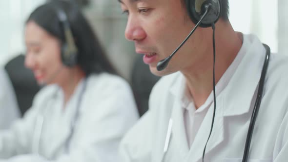 Close Up Of An Asian Man Doctor With Colleagues Working As Call Centre Agent Speaking To Customer