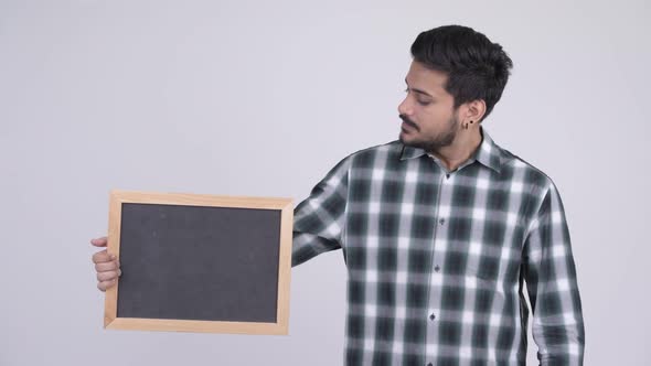 Young Stressed Bearded Indian Man with Blackboard and Giving Thumbs Down