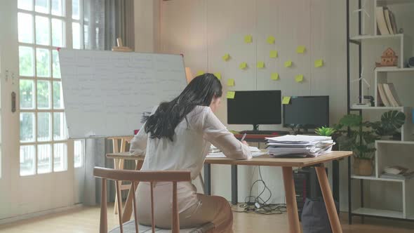 Back View Of Asian Woman Writing Something On Paper While Working With Documents At The Office