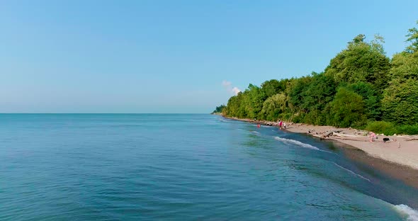 Aerial footage of lake coastline with people playing in the water in the background.