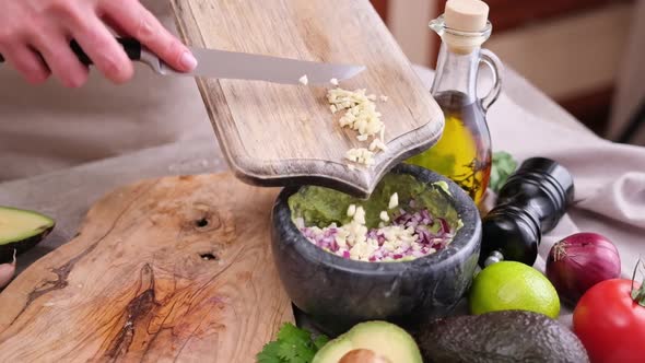 Making Guacamole Sauce  Woman Pouring Chopped Garlic Into Bowl with Mashed Avocado and Onion