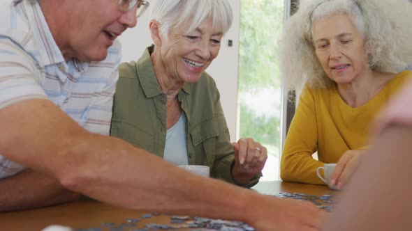 Happy senior diverse people playing puzzle at table at retirement home