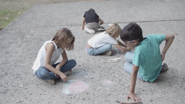 Multiethnic Children Sitting on Asphalt and Drawing with Chalks