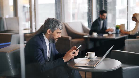 Grey-haired Businessman Touching Smartphone Screen Using Gadget in Cafe