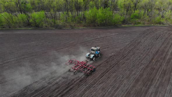 A Tractor with a Harrow Cultivates the Land