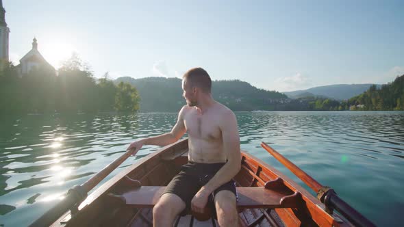 Man Sitting in Wooden Boat Sails Past Island on Bled Lake
