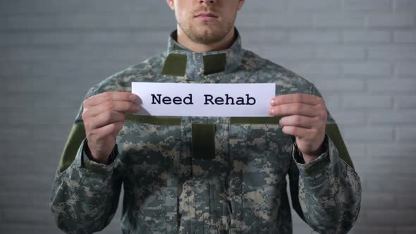 Need Rehab Words Written on Sign in Hands of Male Soldier, Social Support